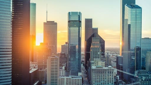 Houston Factoring Companies "Sunset view of a city's skyline with tall skyscrapers reflecting the golden light, symbolizing urban life and business opportunities.
