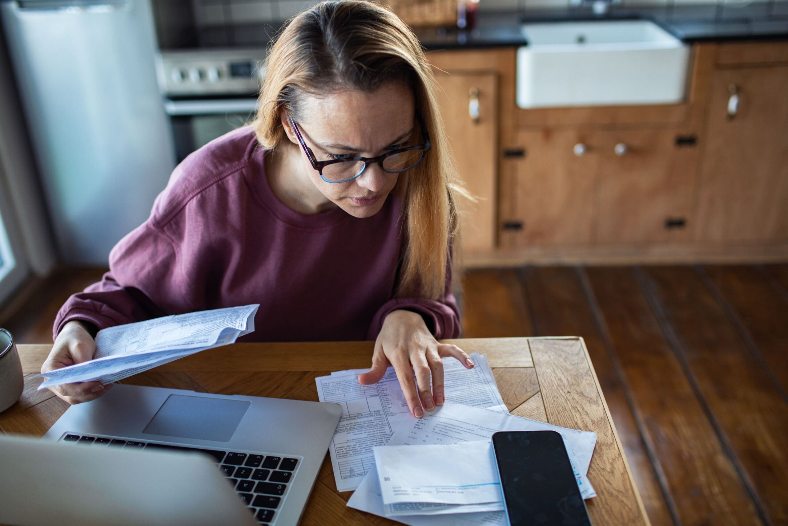 Woman reviewing household bills at home kitchen table Woman reviewing household bills at home kitchen table