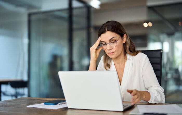Worried fatigued mature business woman wearing glasses having headache at work. Tired busy 40s middle aged businesswoman feeling stress at workplace looking at laptop computer in office.